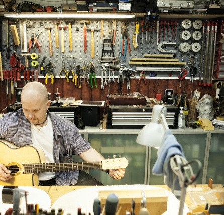 Guitar maker tuning acoustic guitar in workshop
