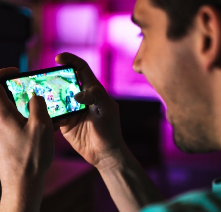 Image closeup of smiling man playing video game on mobile phone